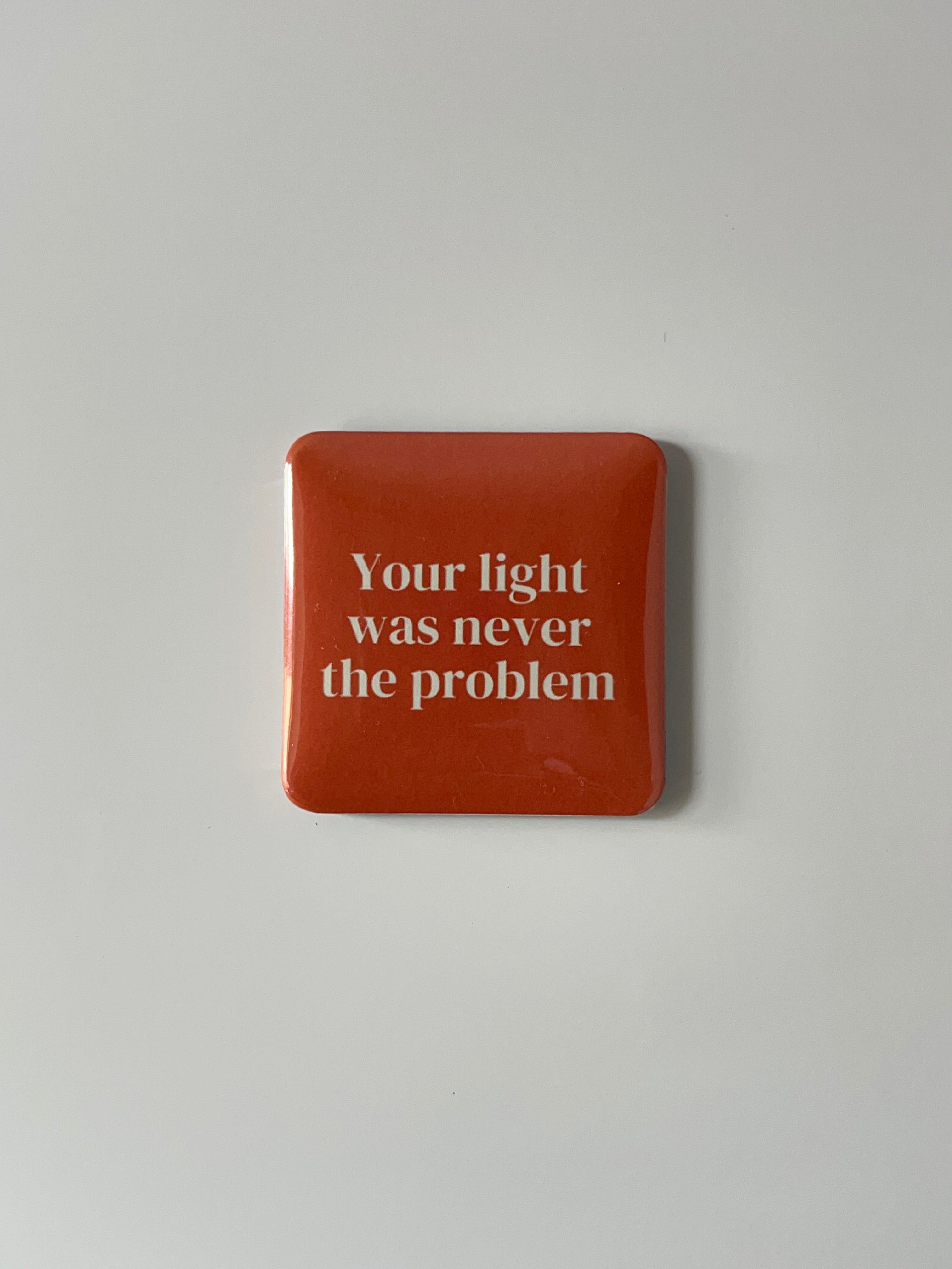 Orange fridge Magnet with text “ Your light was never the Problem “ on a light gray background