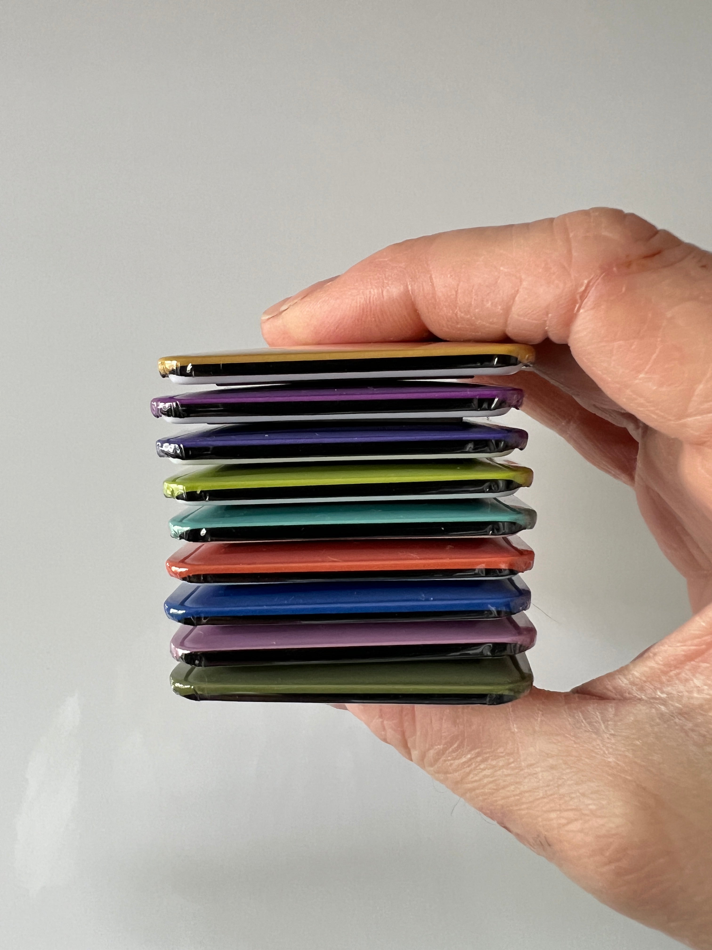 Hand holding a stack of colorful fridge magnets against a plain background