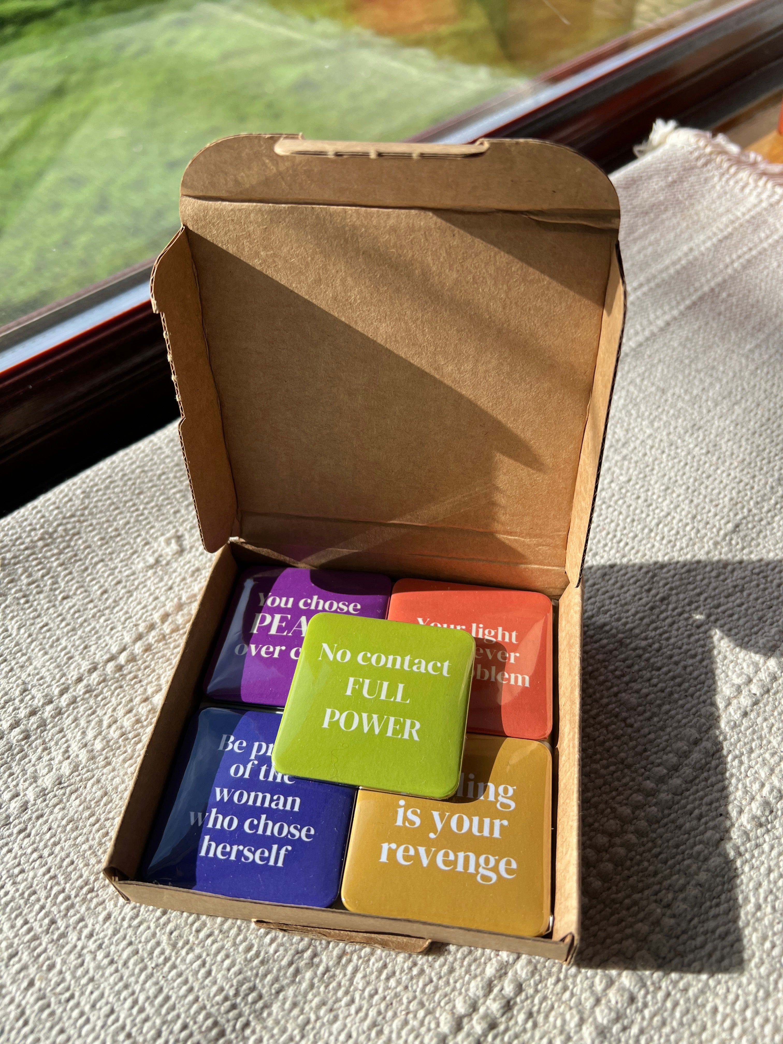 Open cardboard box with colorful motivational fridge magnets inside on a textured surface