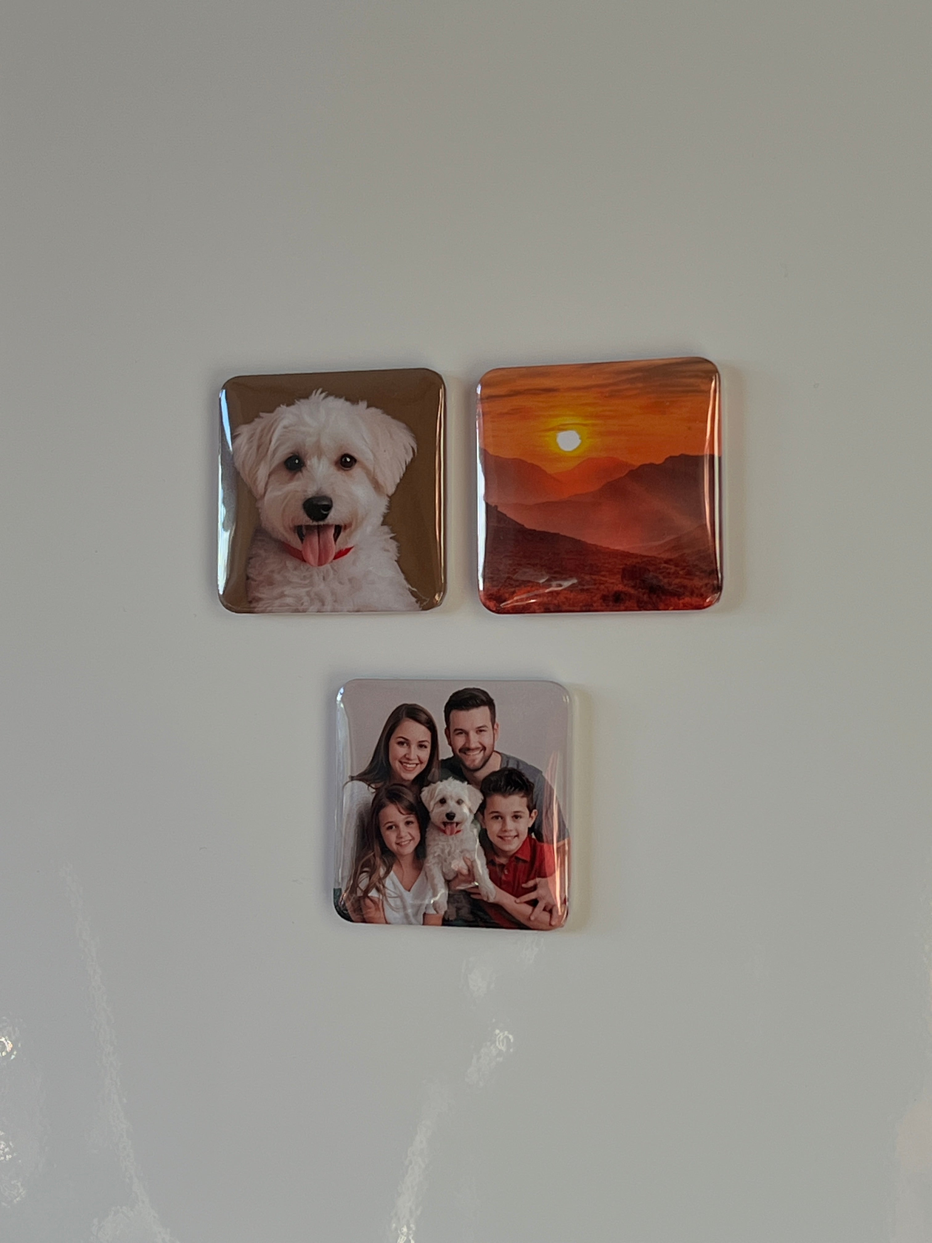 Three square pressed button magnets on a fridge door each with different images.