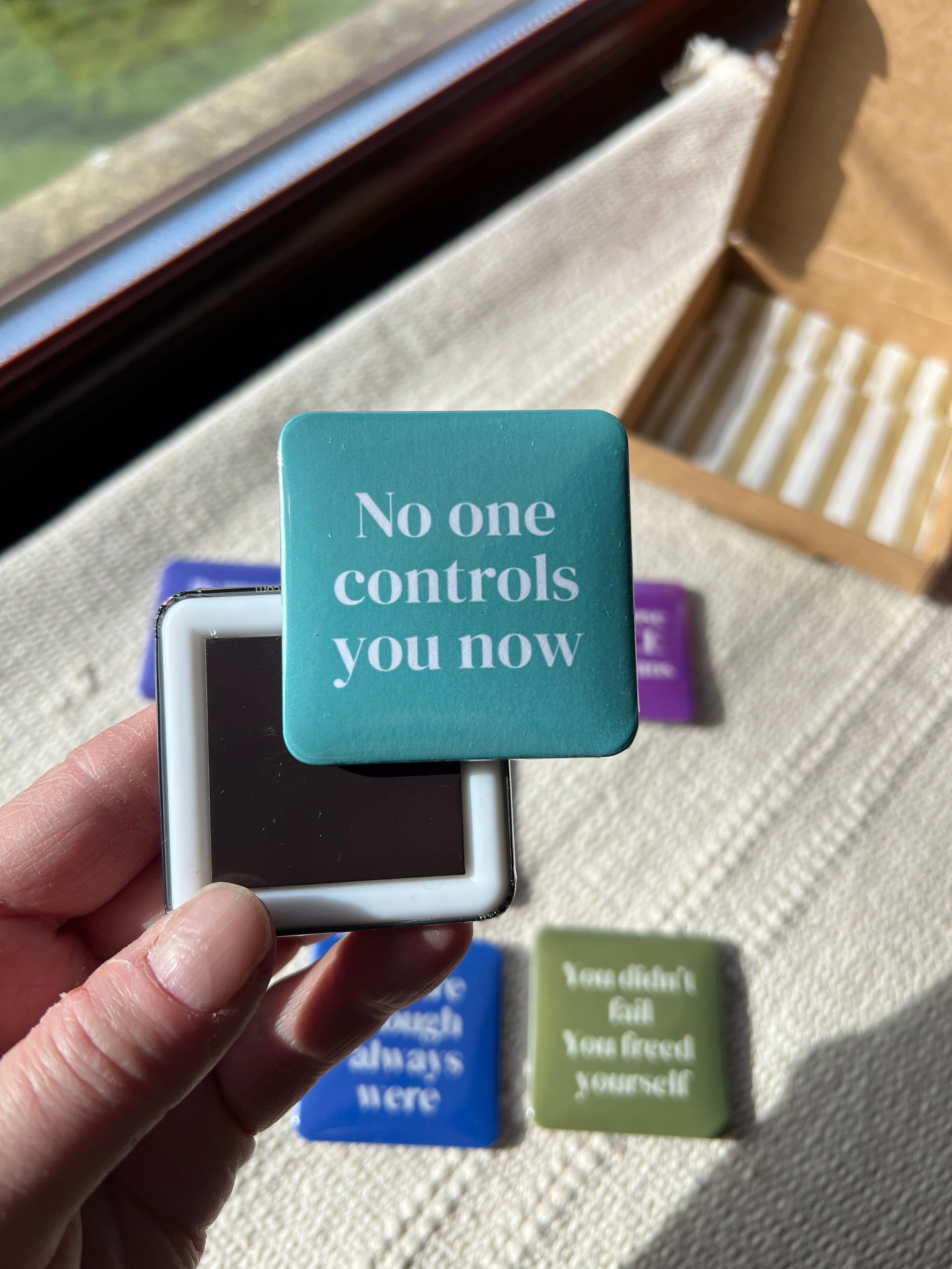 Hand holding a motivational fridge magnet in front of a window