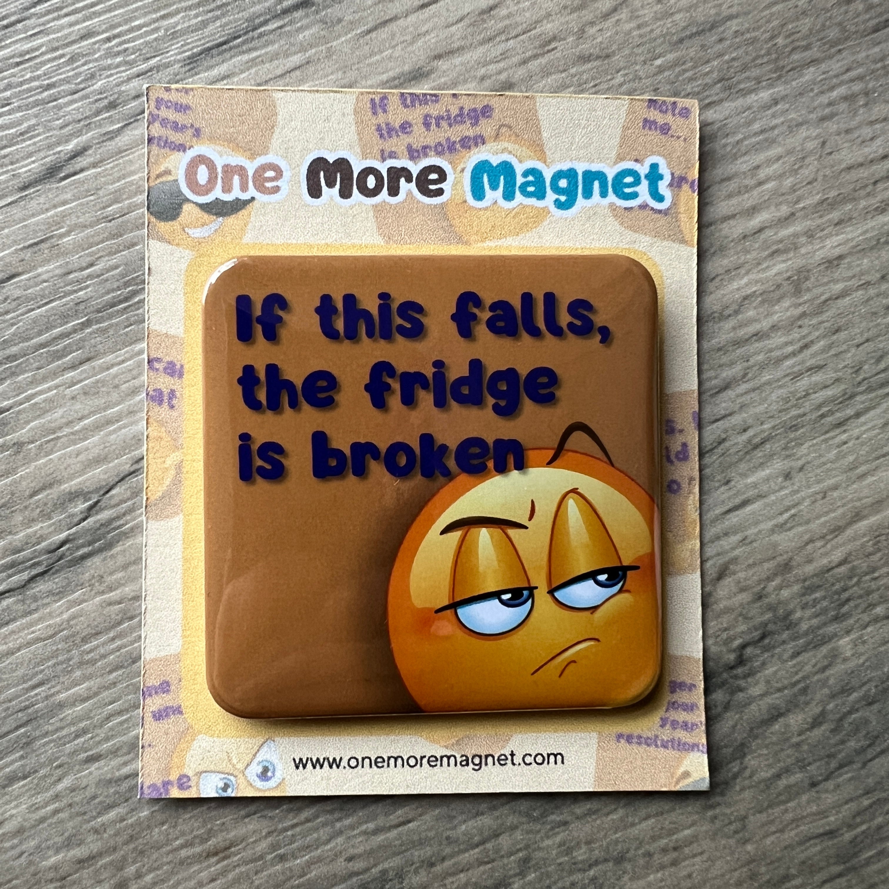 Emoji themed fridge magnet with humorous text on a wooden surface.