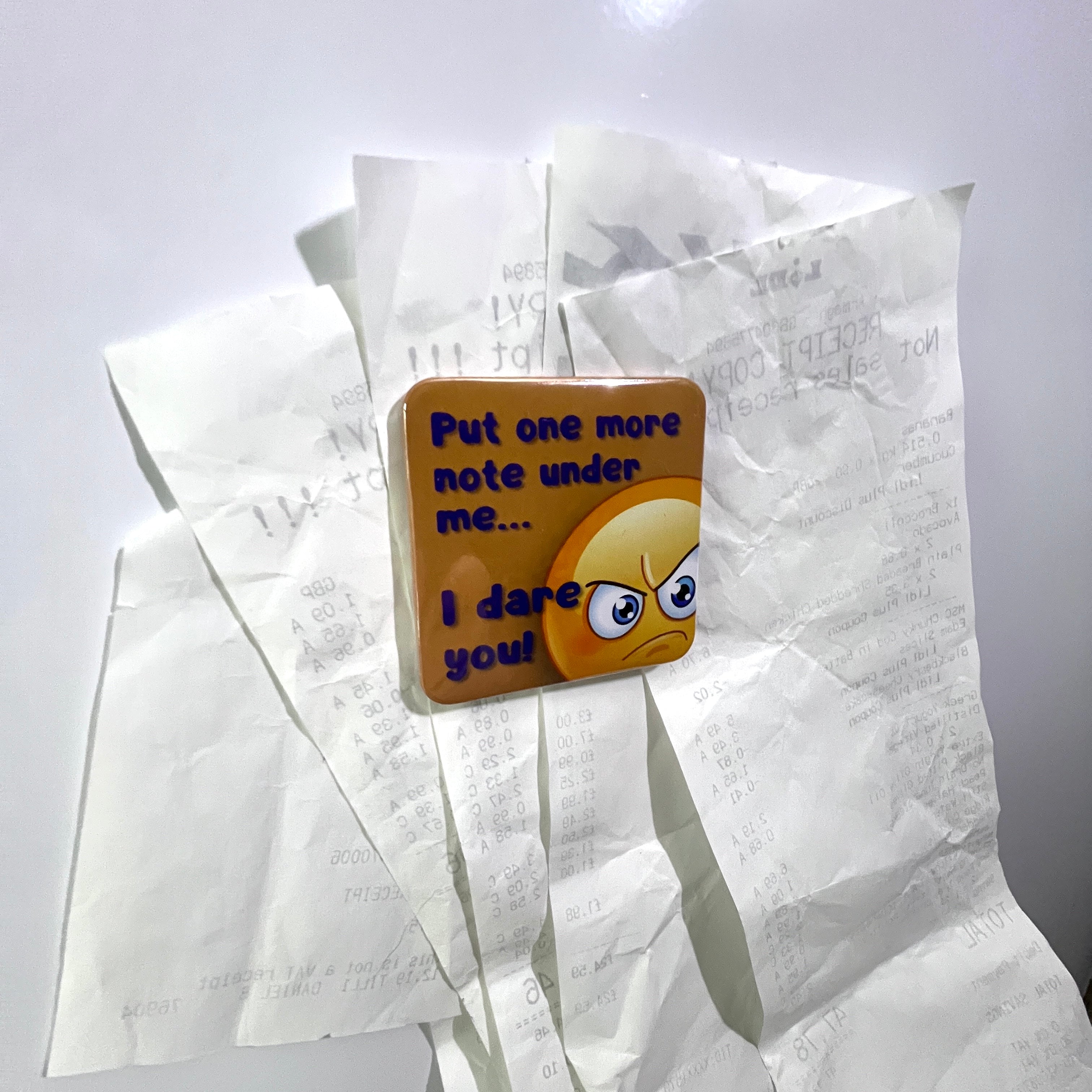 An emoji themed fridge magnet with bills underneath it on the fridge door.